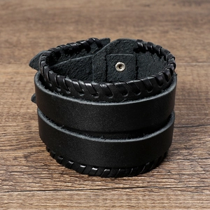 Detailansicht eines schwarzen Lederarmbands mit Webnaht und Metalldruckknöpfen auf Holz