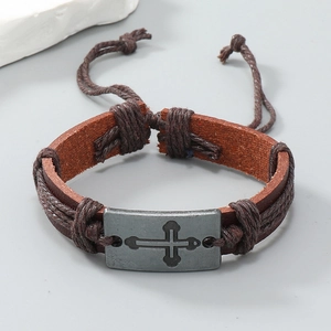 Dettaglio macro del bracciale in pelle marrone intrecciata con ciondolo a croce in lega