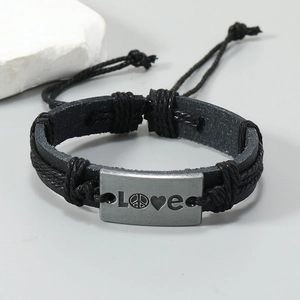 Detail of adjustable woven leather bracelet featuring a vintage LOVE metal plate charm