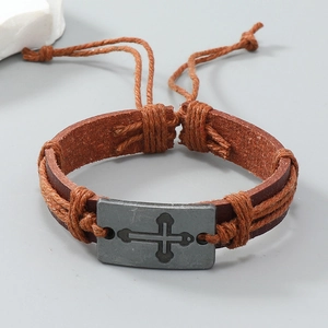 Dettaglio macro del bracciale in pelle marrone intrecciata a mano con croce in metallo