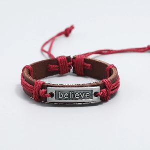 Detail of hand-woven leather bracelet featuring an engraved metal plate with the word believe