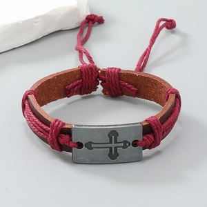 Dettaglio del bracciale in pelle intrecciata retrò con croce in metallo incisa sulla fascia