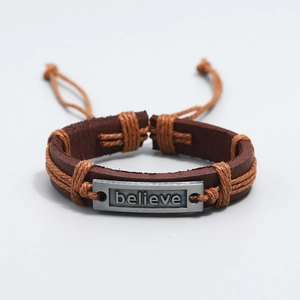 Macro shot of brown braided leather bracelet with believe engraved metal plate