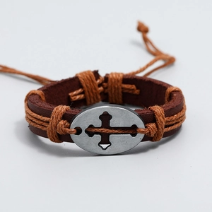 Dettaglio di un bracciale in pelle marrone intrecciata a mano con placca croce in argento