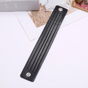 Detail of a minimalist black punk leather bracelet featuring metal snaps and parallel grooves