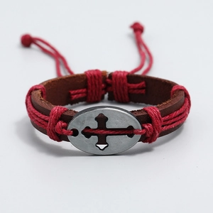 Dettaglio del bracciale in pelle intrecciata con ciondolo a croce e cordini rossi