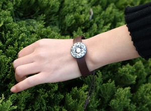 Detail of dark brown braided leather bracelet with ethnic pattern silver metal charm