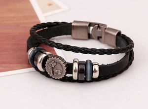 Detail of multi-layer leather bracelet with gear charm and cross wrench metal centerpiece