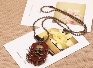 Detail of vintage bronze skull pendant on red leather base with rustic bead chain