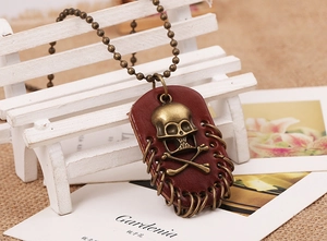Close-up of vintage bronze skull pendant on red leather tag with round bead chain