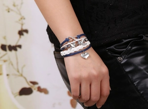 Detail of woven multi-layer bracelet featuring silver sister heart and bird charms