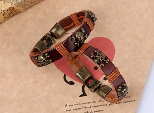 Close-up of vintage leather punk bracelets featuring brass skull charms and wax rope wrap