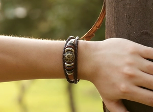 Detail of vintage multilayer braided leather bracelet with sun pattern bronze charm