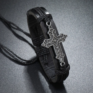 Macro detail of a vintage braided leather bracelet featuring an oxidized silver cross charm