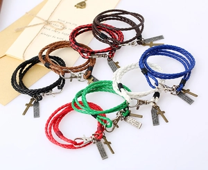 Détail de bracelets en cuir tressé avec breloques en croix et plaques métalliques gravées