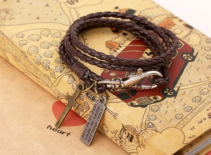 Détail d'un bracelet en cuir tressé marron avec croix en bronze vintage et gravure