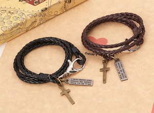 Détail de bracelets en cuir tressé avec croix et plaques en métal gravées en deux couleurs