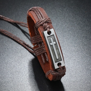 Gros plan sur un bracelet vintage en cuir marron avec pendentif croix en métal et cordons