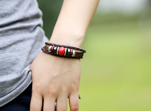 Detail of layered brown braided leather bracelet featuring a red bead and metal rings