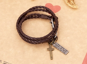Détail du bracelet en cuir tressé marron avec croix en bronze et étiquette gravée