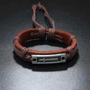 Détail d'un bracelet vintage en cuir marron avec plaque en métal gravée d'une croix