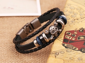 Macro shot of multilayer black leather punk bracelet featuring skull and crossbones charm