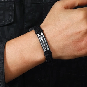 Détail du bracelet en cuir tressé avec plaque de croix en argent sur le poignet