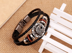 Detail view of multilayer braided leather bracelet with silver eagle emblem on wooden bench