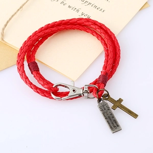 Gros plan sur un bracelet en cuir tressé rouge avec une croix vintage et des charms gravés