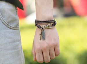Détail d'un bracelet en cuir tressé marron multicouche avec croix et plaque gravée