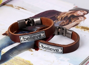 Détail d'un bracelet vintage en cuir marron avec plaque en métal gravée believe