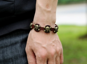 Close-up of punk leather bracelet with bronze skull charms on model wrist outdoors