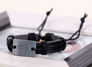 Détail d'un bracelet en cuir noir tressé avec plaque métallique au signe du Cancer