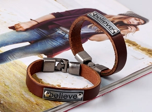 Détail de bracelets en cuir marron avec plaques en métal argenté gravées du mot Believe