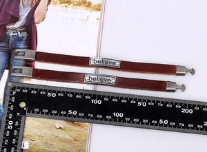Détail des bracelets en cuir avec plaque 'Believe' et règle de mesure graduée