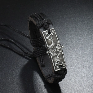 Detail of anchor and helm engraved on vintage metal plate on black leather bracelet