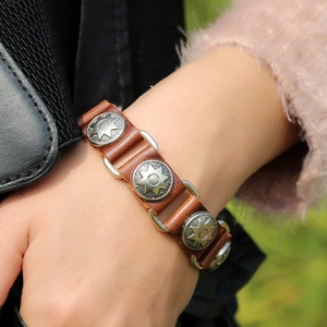 Close-up of a brown leather punk bracelet with three silver sunburst alloy charms