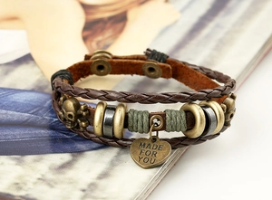 Detail of vintage braided leather bracelet featuring bronze skull and heart pendant