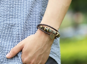 Detail of vintage braided leather bracelet with skull and engraved heart charm