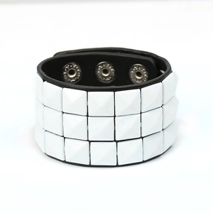 Macro shot of three rows of white pyramid studs on a black faux leather punk bracelet