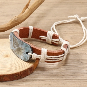 Detail view of woven brown leather bracelet with butterfly print on a rustic wood background