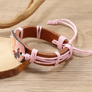 Handmade woven leather bracelet with peace sign and butterfly charm on wood base