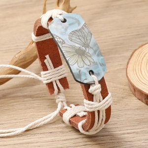 Detail of hand-woven leather bracelet featuring a blue butterfly charm on wood
