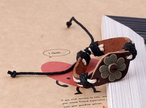 Gros plan d'un bracelet en cuir vintage avec une fleur en bronze et cordons tressés réglables