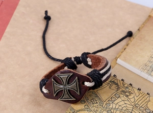 Gros plan sur un bracelet en cuir marron avec croix de fer bronze et détails tressés