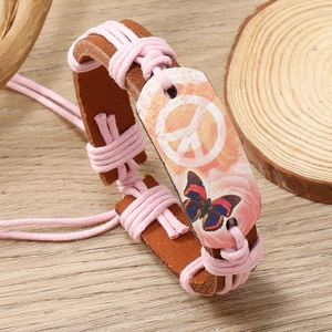Detail of handmade leather bracelet featuring peace sign and butterfly on wood background