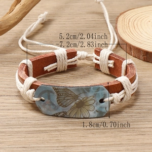 Handmade woven leather bracelet with vintage butterfly and daisy charm on wood