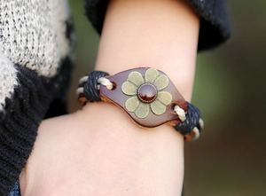 Bracelet en cuir tissé main avec fleur vintage et pierre rouge porté au poignet