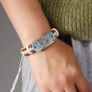 Handmade woven leather bracelet with butterfly and daisy motif on a blue plate charm