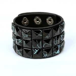 Detail of punk wide black leather bracelet with triple rows of blue splattered square studs